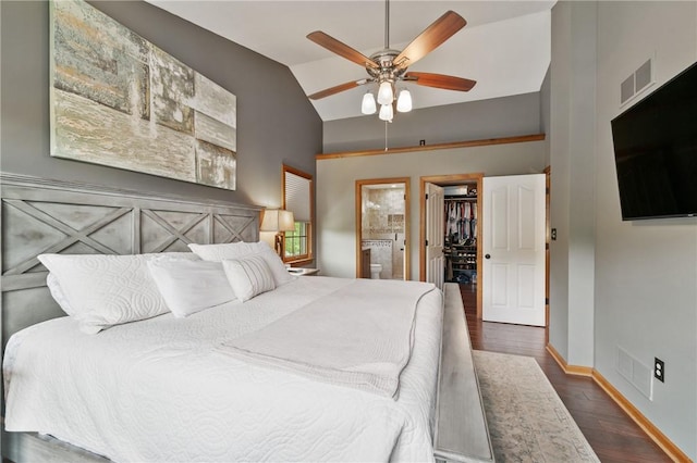 bedroom featuring a walk in closet, lofted ceiling, wood finished floors, ensuite bath, and baseboards