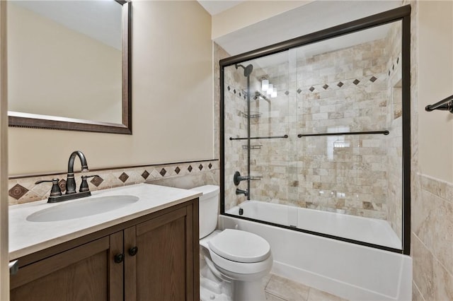 bathroom featuring tile walls, toilet, combined bath / shower with glass door, vanity, and a wainscoted wall