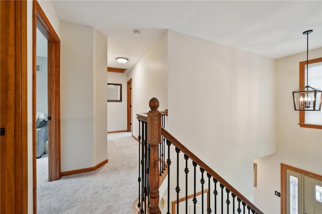 corridor featuring an upstairs landing, light carpet, a chandelier, and baseboards