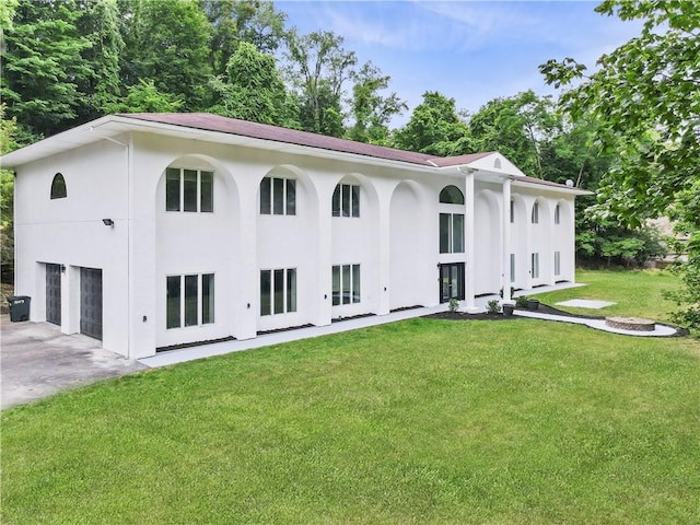 rear view of house featuring concrete driveway, stucco siding, a garage, and a lawn