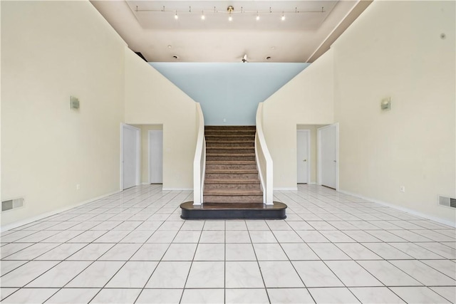 unfurnished living room with a high ceiling, stairs, light tile patterned floors, baseboards, and rail lighting