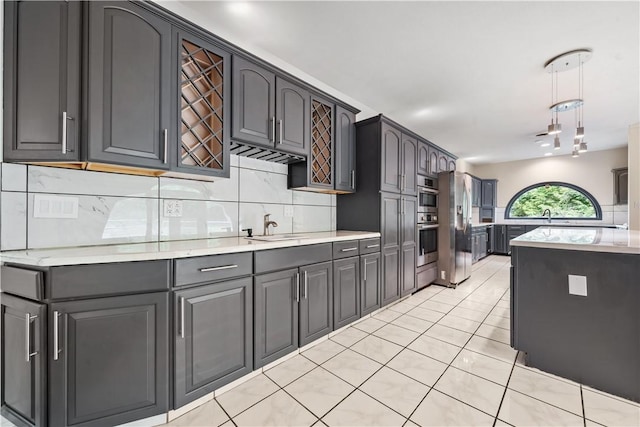 kitchen featuring appliances with stainless steel finishes, a sink, decorative backsplash, light tile patterned flooring, and decorative light fixtures