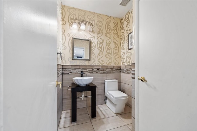 half bath featuring wallpapered walls, toilet, tile walls, tile patterned flooring, and vanity