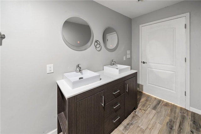 full bath featuring wood finished floors, double vanity, and baseboards