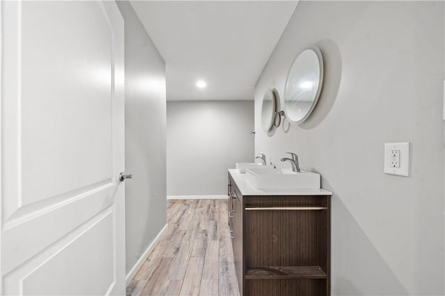 bathroom with wood finished floors, double vanity, baseboards, and recessed lighting