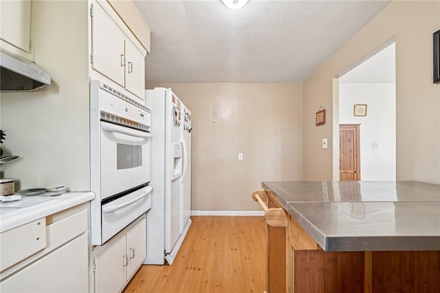 kitchen with a warming drawer, white appliances, light wood finished floors, light countertops, and white cabinetry