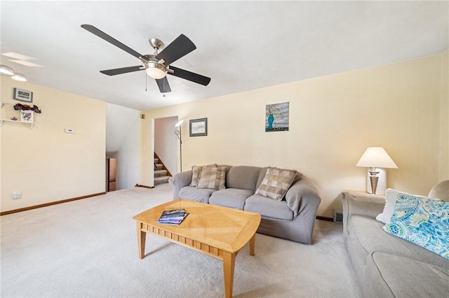 living area with light colored carpet, stairs, a ceiling fan, and baseboards