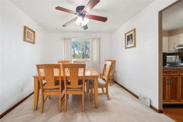 dining area with a ceiling fan, baseboards, and light colored carpet