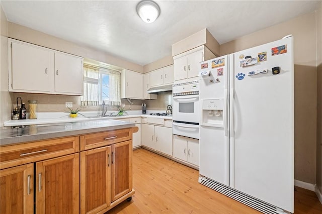 kitchen with white appliances, a warming drawer, light wood-style floors, and under cabinet range hood