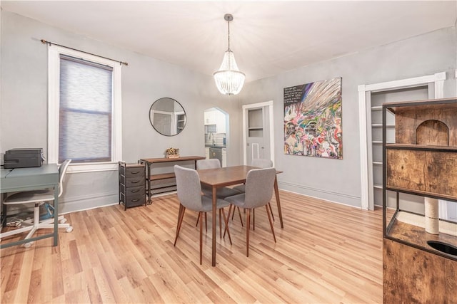 dining space with light wood-type flooring, a chandelier, baseboards, arched walkways, and an office area