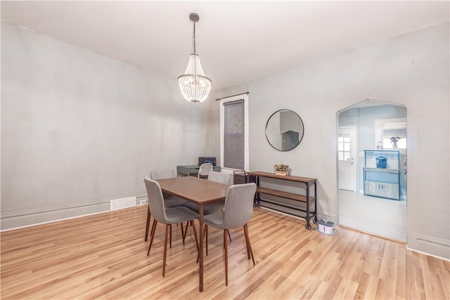 dining space featuring a chandelier, light wood finished floors, arched walkways, and baseboards