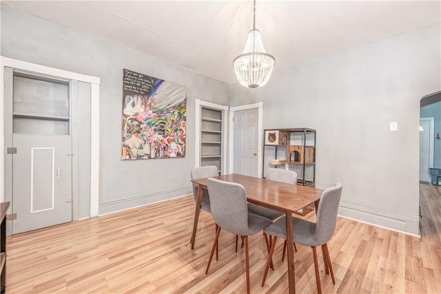 dining area featuring light wood finished floors, a chandelier, arched walkways, and baseboards