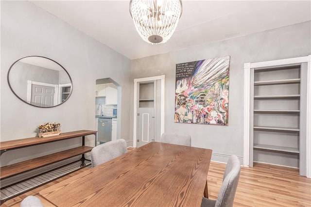 dining space with light wood-style floors, a chandelier, arched walkways, and baseboards