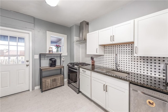 kitchen featuring stainless steel appliances, wall chimney exhaust hood, a sink, white cabinetry, and dark stone countertops
