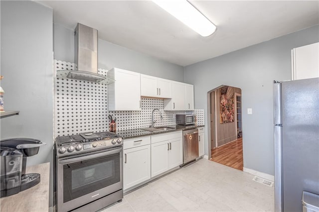 kitchen featuring stainless steel appliances, wall chimney exhaust hood, a sink, white cabinetry, and arched walkways