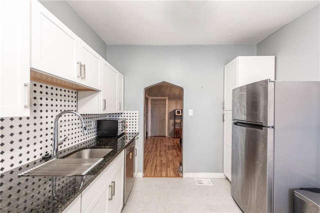 kitchen featuring stainless steel appliances, arched walkways, dark stone counters, and white cabinets