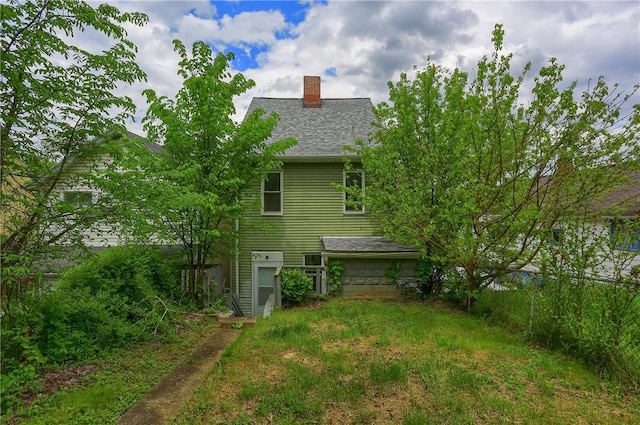 back of house with a chimney and a shingled roof
