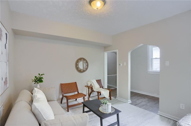 living room featuring arched walkways, wood finished floors, and baseboards