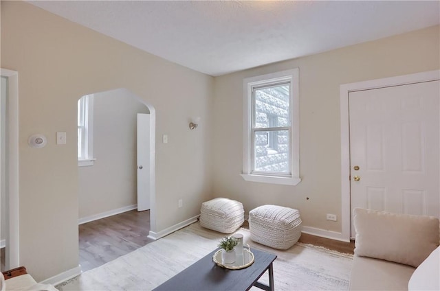 living area with wood finished floors, arched walkways, and baseboards