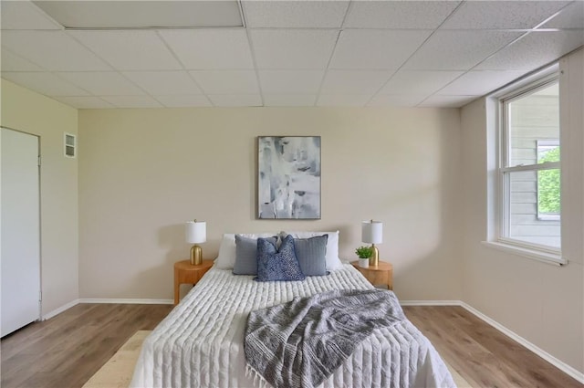 bedroom featuring wood finished floors, a paneled ceiling, and baseboards