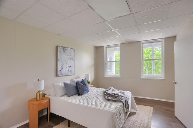 bedroom with a paneled ceiling, wood finished floors, and baseboards