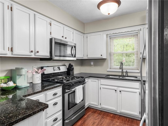 kitchen featuring stainless steel appliances, a sink, white cabinetry, a textured ceiling, and dark stone counters
