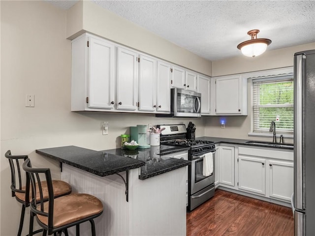 kitchen featuring stainless steel appliances, a sink, a peninsula, dark wood finished floors, and dark stone counters