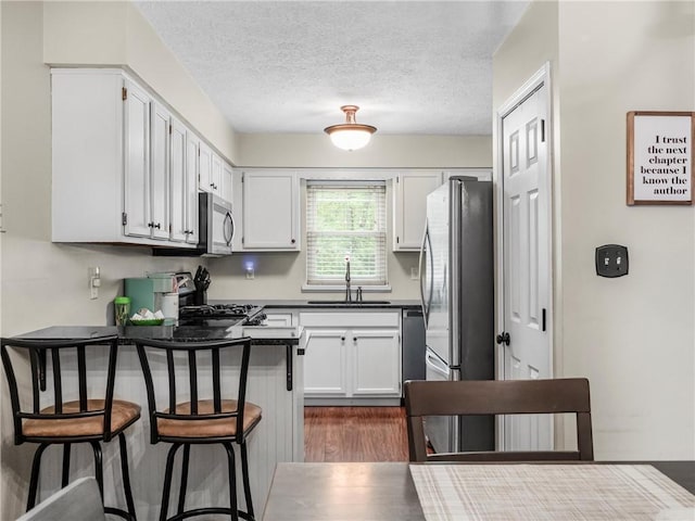 kitchen featuring appliances with stainless steel finishes, a sink, dark countertops, a peninsula, and dark wood-style floors