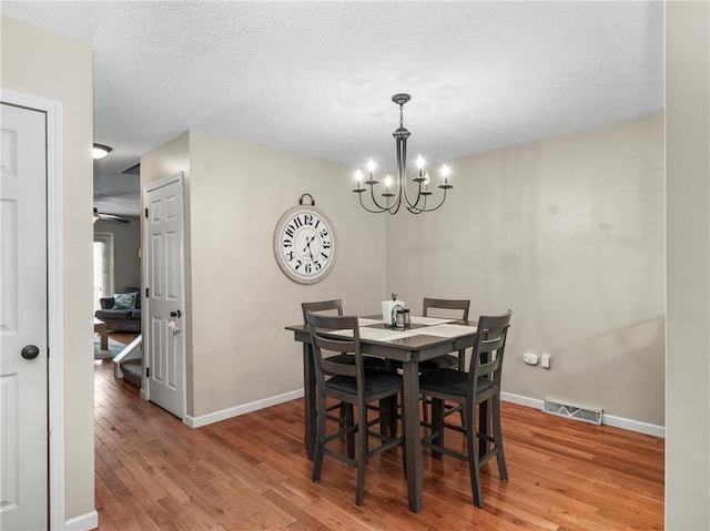 dining area featuring light wood-style flooring, a chandelier, baseboards, and a textured ceiling
