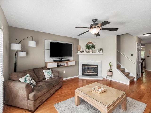 living area featuring wood finished floors, ceiling fan, a premium fireplace, and stairs