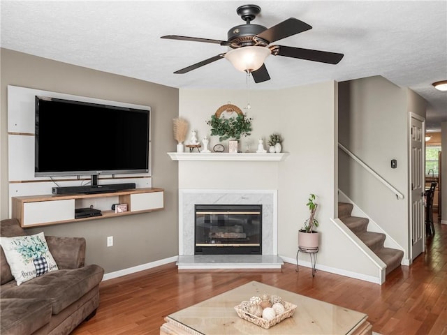 living area featuring wood finished floors, a ceiling fan, a premium fireplace, stairs, and baseboards