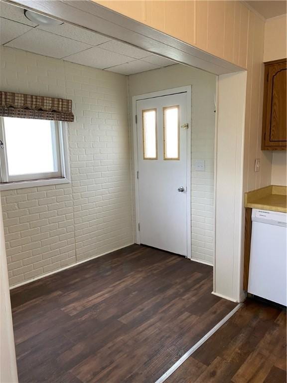 entryway with brick wall, dark wood-style flooring, and a drop ceiling