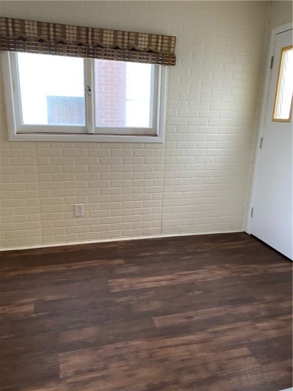 unfurnished room with dark wood-style flooring and brick wall