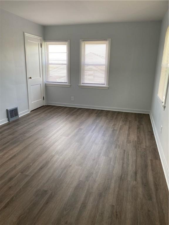 empty room featuring dark wood-type flooring, plenty of natural light, and baseboards