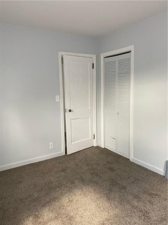 unfurnished bedroom featuring dark carpet, a closet, and baseboards