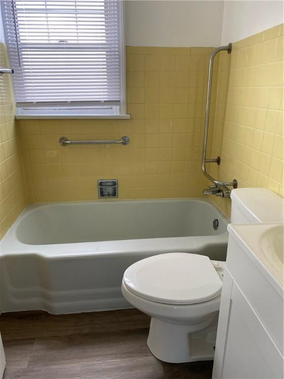 full bath featuring wood finished floors, a tub to relax in, toilet, vanity, and a shower