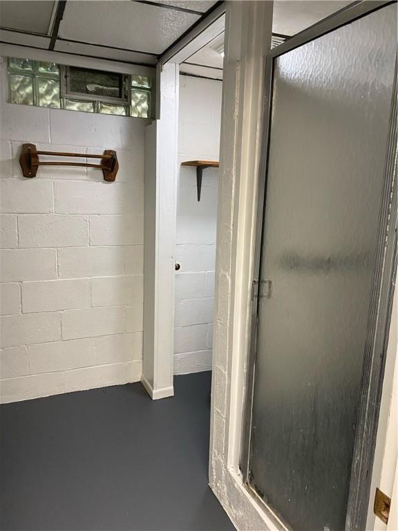 full bath featuring a shower stall, finished concrete flooring, and concrete block wall