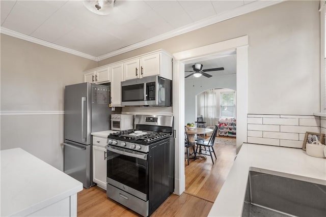 kitchen featuring appliances with stainless steel finishes, light countertops, white cabinets, crown molding, and light wood finished floors
