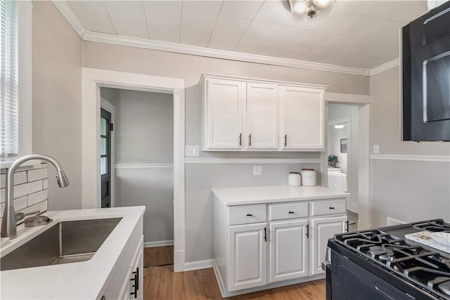 kitchen with gas stove, a sink, white cabinetry, ornamental molding, and light countertops