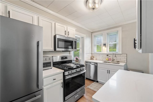 kitchen featuring stainless steel appliances, a sink, crown molding, tasteful backsplash, and light countertops
