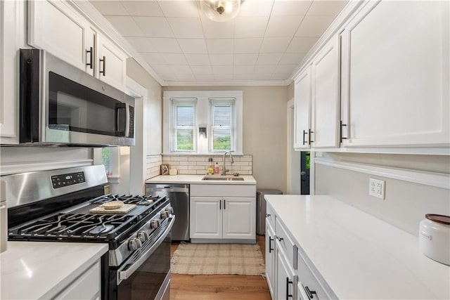 kitchen featuring appliances with stainless steel finishes, a sink, white cabinetry, light wood-type flooring, and crown molding