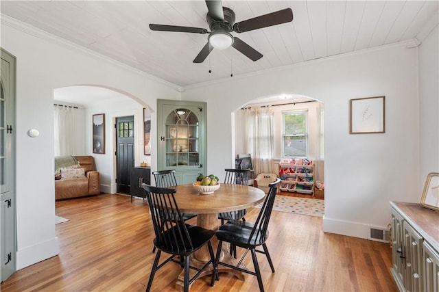 dining room featuring arched walkways, light wood-style flooring, a ceiling fan, ornamental molding, and baseboards