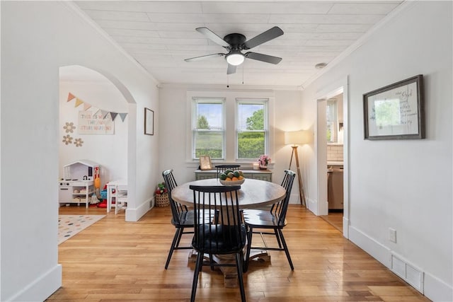 dining area with a ceiling fan, ornamental molding, light wood finished floors, arched walkways, and baseboards