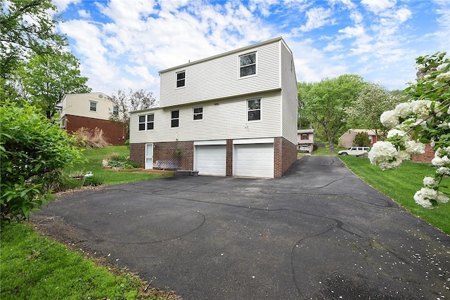 rear view of property with brick siding, an attached garage, and asphalt driveway