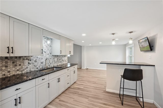 kitchen with a sink, decorative backsplash, baseboards, light wood finished floors, and recessed lighting