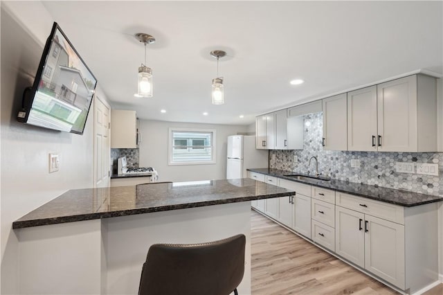 kitchen featuring a sink, freestanding refrigerator, decorative backsplash, light wood-type flooring, and recessed lighting