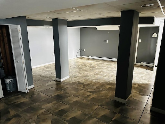 basement with a baseboard heating unit, baseboards, a paneled ceiling, and dark tile patterned flooring