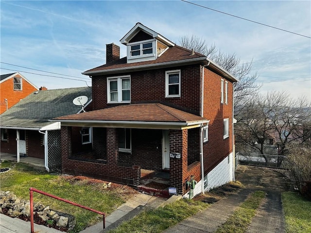 american foursquare style home featuring a chimney, brick siding, and a porch