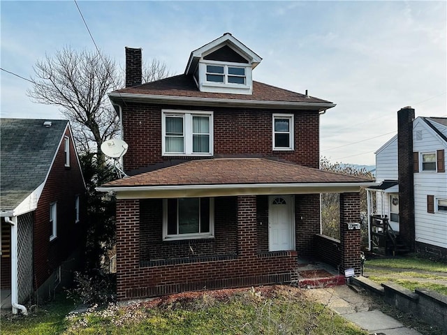 american foursquare style home featuring brick siding, covered porch, a chimney, and a shingled roof