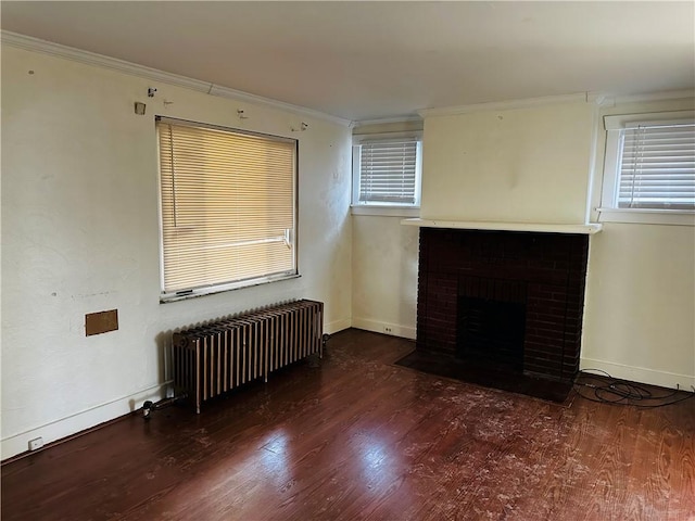 unfurnished living room with radiator, wood finished floors, ornamental molding, baseboards, and a brick fireplace